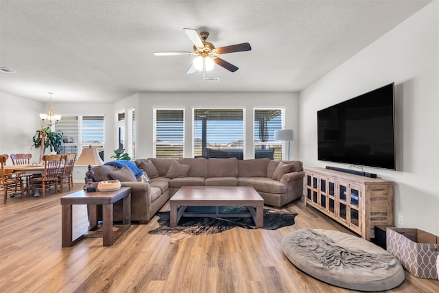 living room with light hardwood / wood-style flooring, ceiling fan with notable chandelier, and a textured ceiling