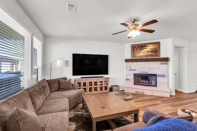 living room with a stone fireplace, ceiling fan, plenty of natural light, and hardwood / wood-style flooring