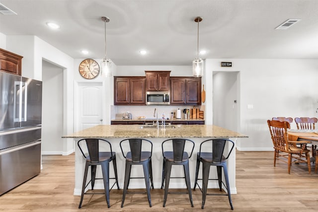 kitchen with stainless steel appliances, sink, pendant lighting, a center island with sink, and light hardwood / wood-style flooring