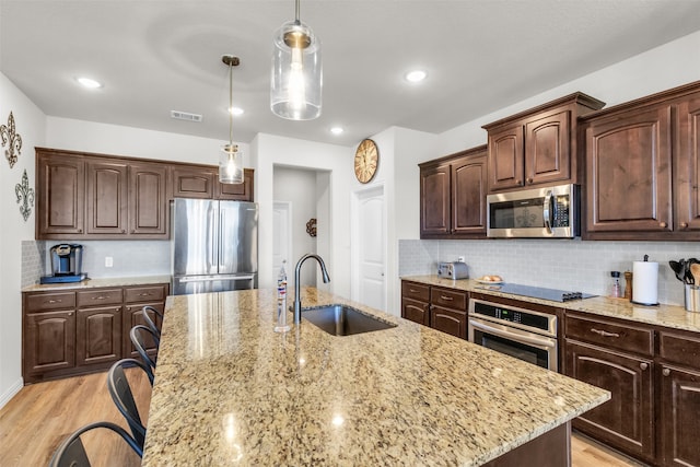 kitchen with dark brown cabinets, stainless steel appliances, sink, decorative light fixtures, and light hardwood / wood-style flooring