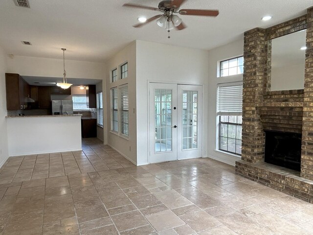 unfurnished living room with ceiling fan, a textured ceiling, a brick fireplace, and french doors