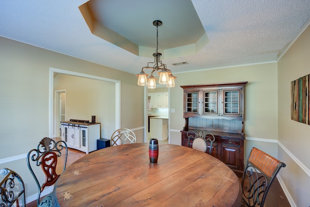 dining area featuring a textured ceiling, a tray ceiling, ornamental molding, hardwood / wood-style floors, and a chandelier