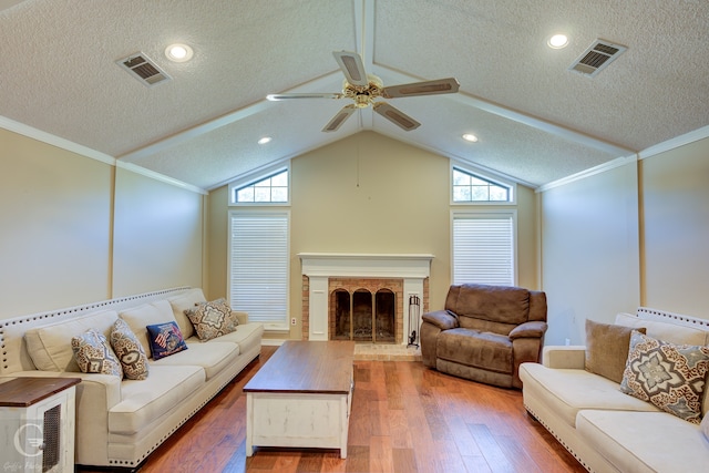 living room featuring a brick fireplace, hardwood / wood-style flooring, ornamental molding, and a textured ceiling