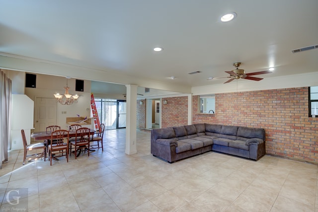 tiled living room with ceiling fan with notable chandelier and brick wall