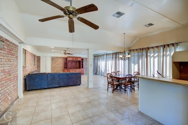 tiled dining space featuring a healthy amount of sunlight, lofted ceiling, ceiling fan with notable chandelier, and brick wall