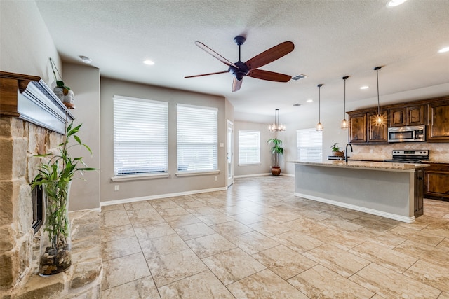 kitchen with a textured ceiling, appliances with stainless steel finishes, tasteful backsplash, light stone counters, and a center island with sink