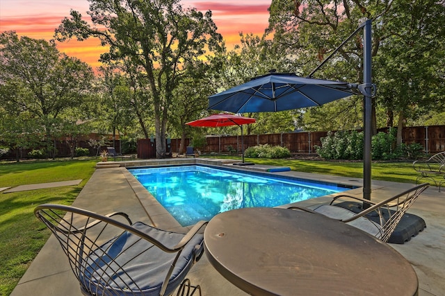 pool at dusk featuring a yard and a patio