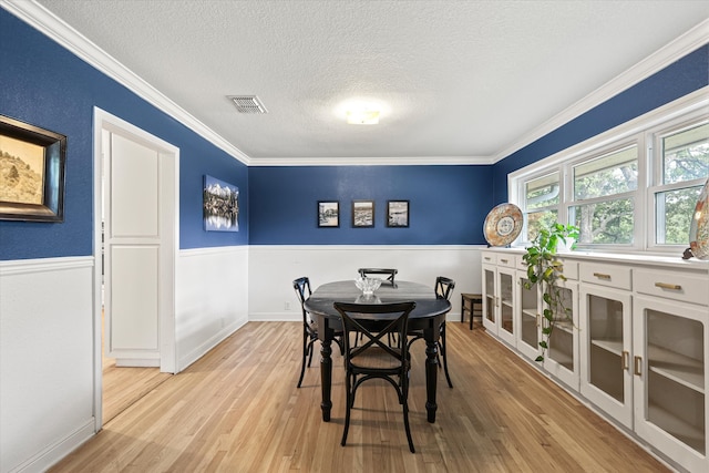 dining area with a textured ceiling, light wood-type flooring, and ornamental molding