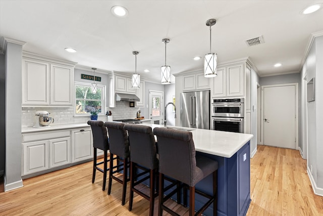 kitchen featuring light hardwood / wood-style floors, a kitchen island with sink, sink, stainless steel appliances, and decorative light fixtures