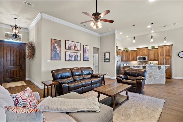 living room featuring ceiling fan with notable chandelier, light hardwood / wood-style flooring, and ornamental molding