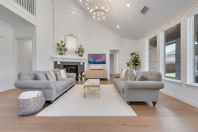 living room with a fireplace, high vaulted ceiling, light hardwood / wood-style flooring, and an inviting chandelier