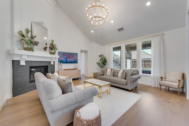 living room featuring an inviting chandelier, light hardwood / wood-style floors, a brick fireplace, and high vaulted ceiling