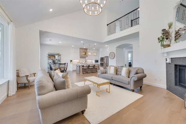 living room with sink, light hardwood / wood-style flooring, a towering ceiling, a fireplace, and a notable chandelier