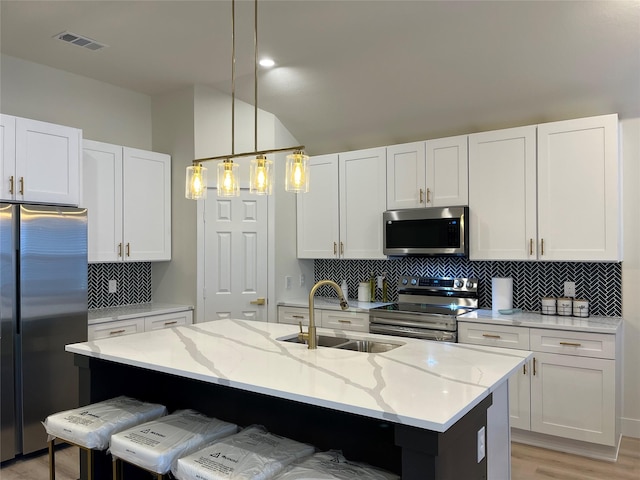 kitchen with stainless steel appliances, white cabinetry, hanging light fixtures, and a center island with sink