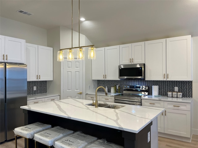 214 E 15th Ave, Corsicana, TX 75110 - kitchen with appliances with stainless steel finishes, a kitchen island with sink, tasteful backsplash, light stone counters, and white cabinetry
