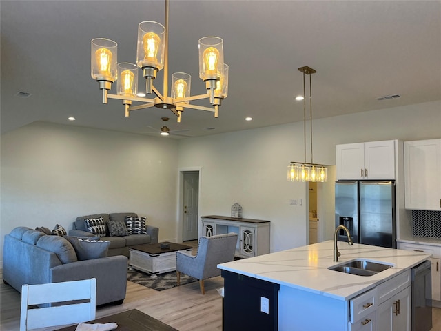 kitchen featuring decorative light fixtures, an island with sink, sink, white cabinets, and stainless steel refrigerator with ice dispenser