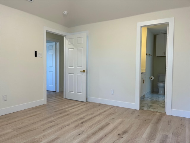 unfurnished bedroom featuring ensuite bath and light hardwood / wood-style flooring