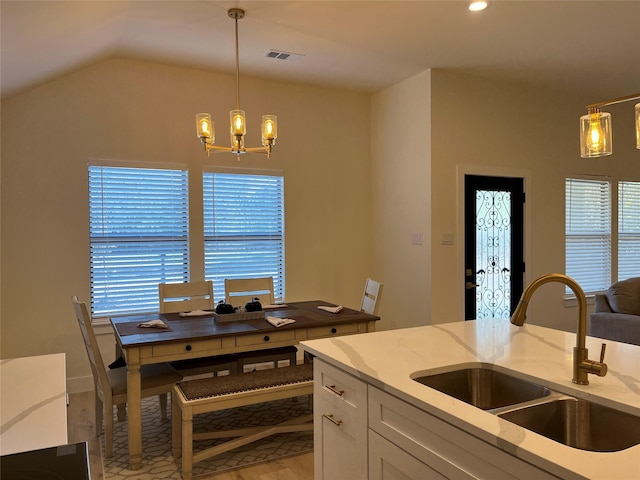 kitchen featuring sink, light stone countertops, white cabinets, decorative light fixtures, and vaulted ceiling