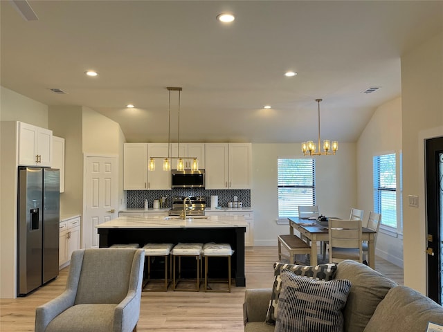 kitchen featuring a kitchen island with sink, hanging light fixtures, white cabinets, and appliances with stainless steel finishes