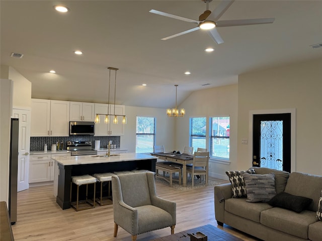 living room featuring ceiling fan with notable chandelier, lofted ceiling, light hardwood / wood-style floors, and sink