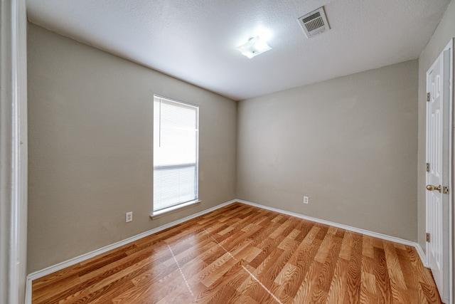 spare room with a textured ceiling and light hardwood / wood-style flooring