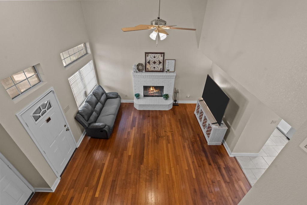 living room featuring a fireplace, a towering ceiling, dark hardwood / wood-style floors, and ceiling fan