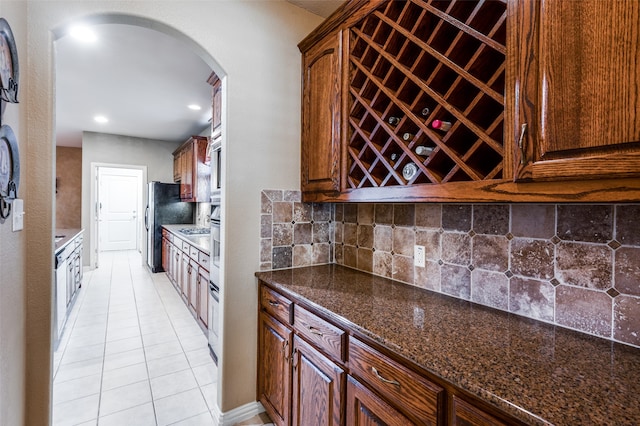 kitchen with dark stone counters, light tile patterned flooring, stainless steel fridge, and decorative backsplash