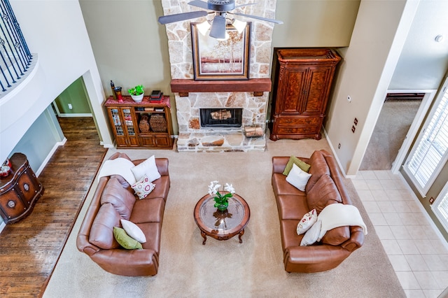 living room featuring a stone fireplace, tile patterned floors, ceiling fan, and a towering ceiling