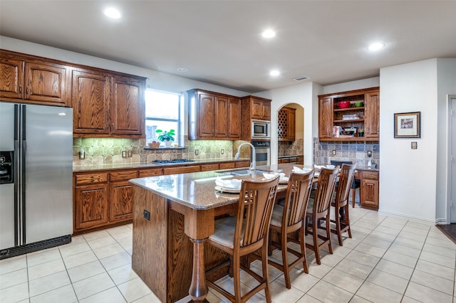 kitchen with an island with sink, a kitchen bar, backsplash, and appliances with stainless steel finishes