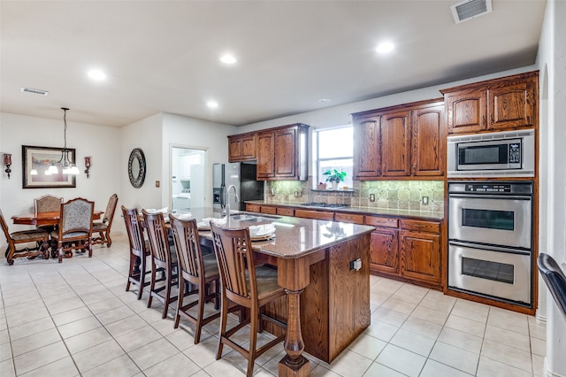 kitchen featuring sink, appliances with stainless steel finishes, light stone countertops, an island with sink, and a notable chandelier