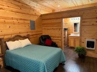 bedroom featuring electric panel, heating unit, ensuite bath, dark hardwood / wood-style floors, and wood walls