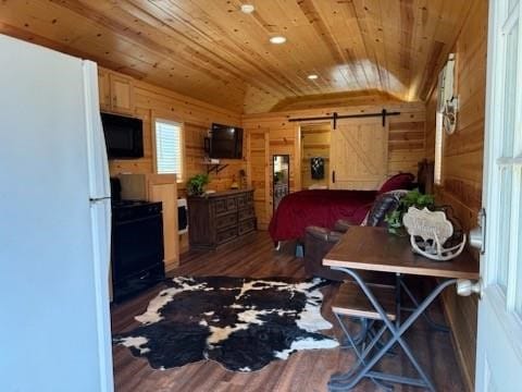 bedroom with white refrigerator, a barn door, dark hardwood / wood-style flooring, wood walls, and lofted ceiling