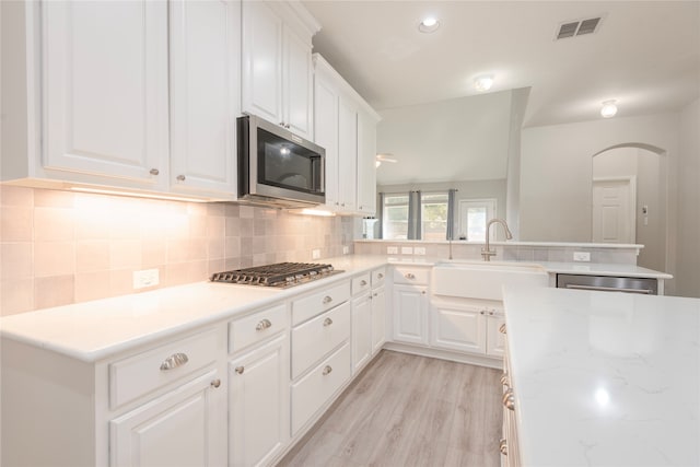 kitchen featuring stainless steel appliances, backsplash, sink, white cabinets, and light hardwood / wood-style floors