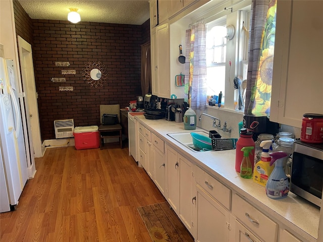 kitchen with white cabinetry, sink, white refrigerator with ice dispenser, light hardwood / wood-style floors, and a textured ceiling