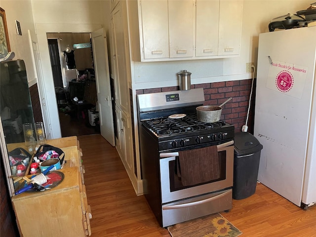 kitchen with white cabinetry, fridge, stainless steel range with gas stovetop, and light wood-type flooring