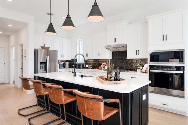 kitchen with hanging light fixtures, stainless steel appliances, an island with sink, and white cabinets