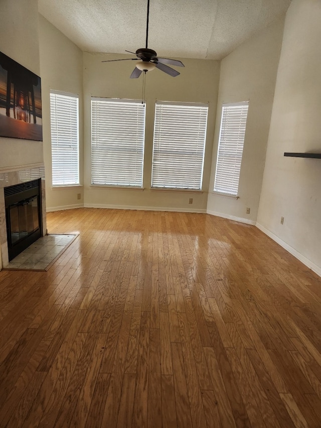 unfurnished living room featuring lofted ceiling, light hardwood / wood-style floors, ceiling fan, and a textured ceiling