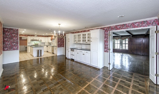 kitchen featuring a textured ceiling, decorative light fixtures, white cabinetry, a center island, and crown molding