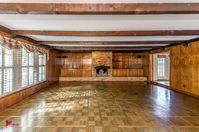 unfurnished living room with a fireplace, wooden walls, beamed ceiling, and dark parquet flooring