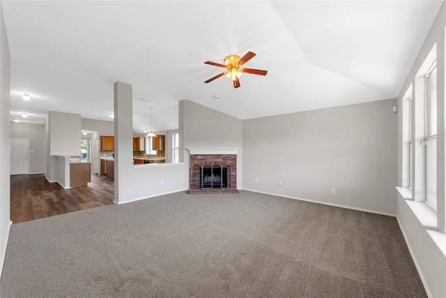 unfurnished living room with ceiling fan, a brick fireplace, a wealth of natural light, and dark colored carpet