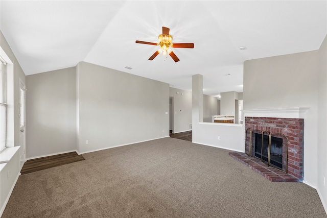 unfurnished living room featuring a fireplace, dark carpet, lofted ceiling, and ceiling fan