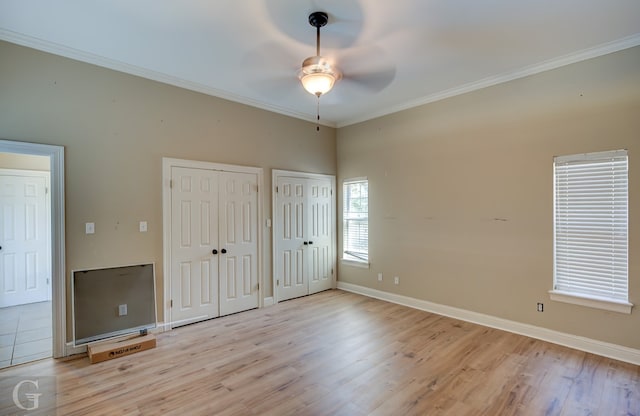 unfurnished bedroom with ornamental molding, light wood-type flooring, two closets, and ceiling fan