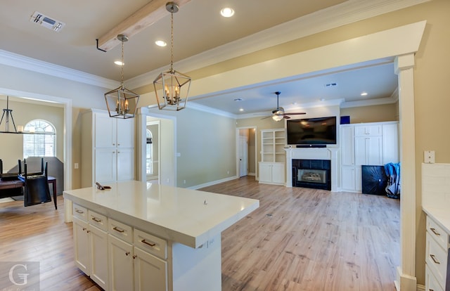 kitchen with light wood-type flooring, white cabinetry, hanging light fixtures, a fireplace, and a kitchen island