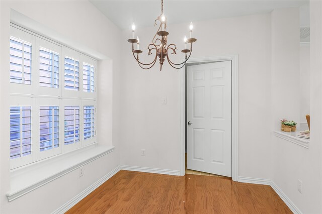 unfurnished dining area featuring an inviting chandelier and hardwood / wood-style flooring