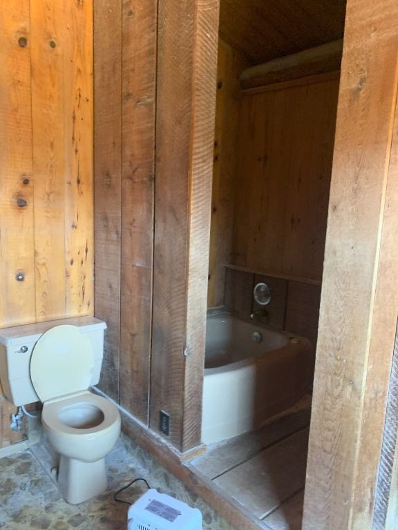 bathroom featuring wooden walls, toilet, and a tub