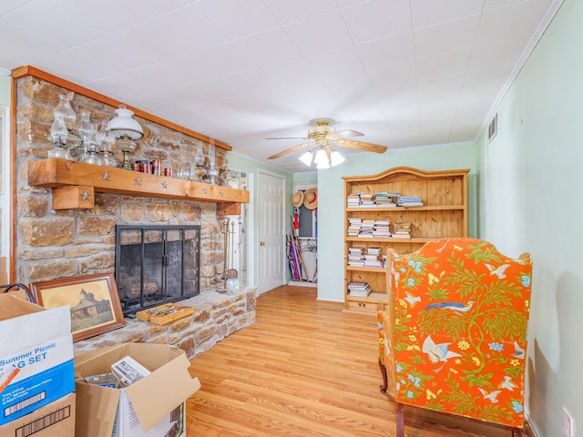 living room with ceiling fan, a stone fireplace, light wood-type flooring, and ornamental molding