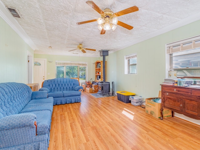 living room featuring ceiling fan, light wood-type flooring, crown molding, and a wood stove