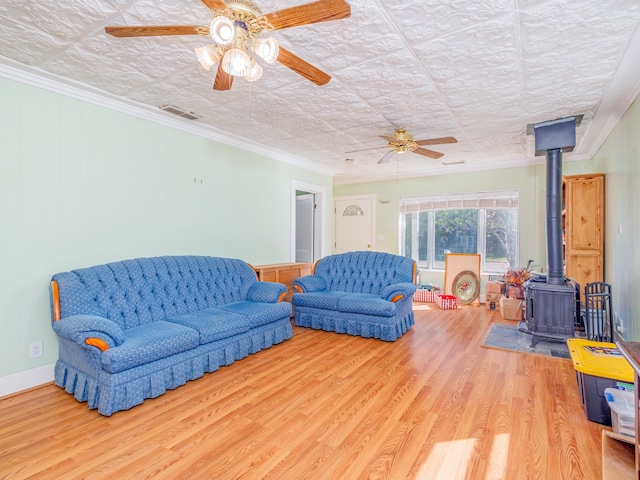 living room featuring a wood stove, a textured ceiling, wood-type flooring, ceiling fan, and ornamental molding