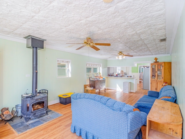 living room featuring ornamental molding, a wood stove, ceiling fan, and hardwood / wood-style floors