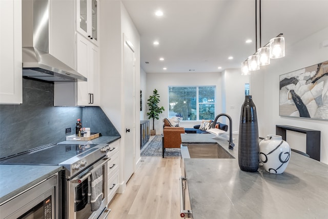 kitchen with white cabinets, hanging light fixtures, sink, wall chimney range hood, and appliances with stainless steel finishes